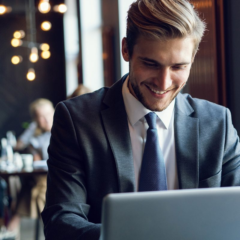 Attractive businessman using a laptop and smiling while working in cafe.